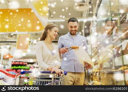 food, sale, consumerism and people concept - happy couple with shopping cart at grocery store or supermarket baking department buying buns or pies over snow. happy couple with shopping cart at grocery store