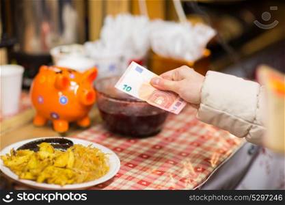 food sale, payment and eating concept - hand with money paying for braised cabbage, potato and sausages with cranberry sauce at street market. hand with money paying food at street market