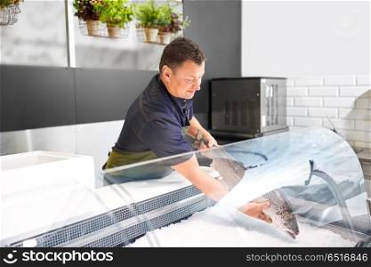 food sale, small business and people concept - male seller putting trout to fridge at fish shop. male seller putting trout to fridge at fish shop. male seller putting trout to fridge at fish shop