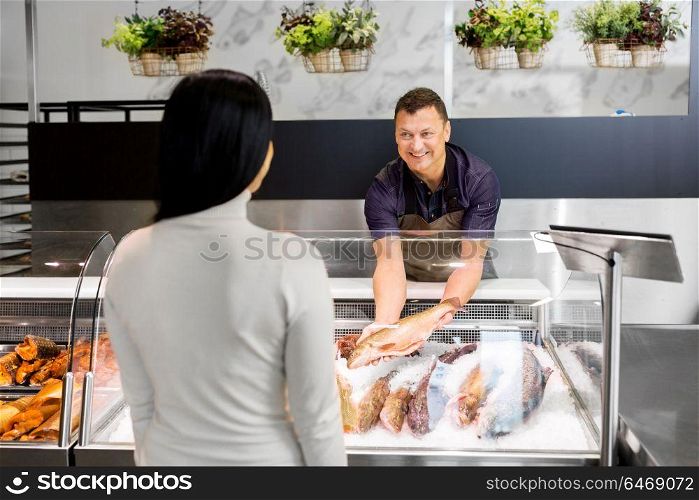 food sale, small business and people concept - male seller showing seafood to female customer at fish shop fridge. seller showing seafood to customer at fish shop