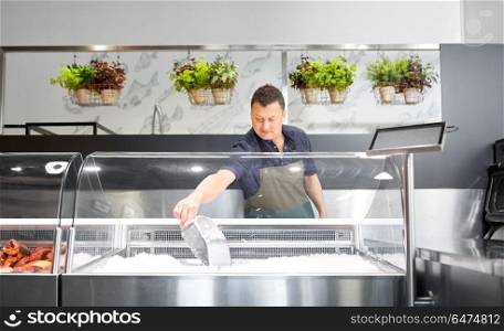 food sale, small business and people concept - male seller with scoop adding ice to fridge at fish shop. male seller adding ice to fridge at fish shop. male seller adding ice to fridge at fish shop