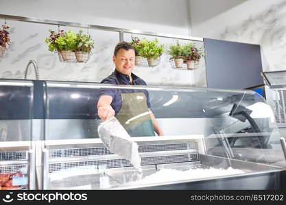 food sale, small business and people concept - male seller with scoop adding ice to fridge at grocery store. male seller adding ice to fridge at grocery store. male seller adding ice to fridge at grocery store