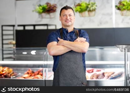 food sale, small business and people concept - male seller with seafood at fish shop fridge. male seller with seafood at fish shop fridge