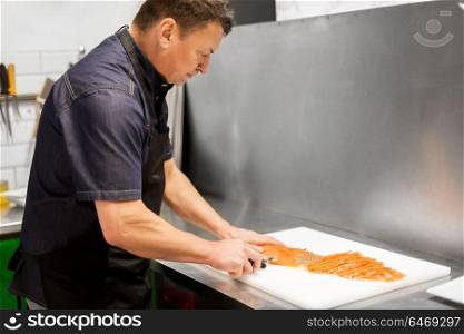 food sale, small business and seafood cooking concept - male or chief slicing smoked salmon fillet at fish shop or restaurant kitchen. man slicing smoked salmon fish fillet