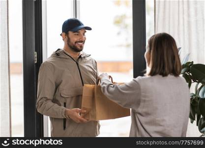 food shipping and people concept - happy delivery man giving paper bag to female customer at home. food delivery man giving order to female customer
