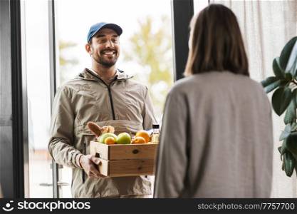 food shipping and people concept - happy delivery man giving wooden box with groceries to female customer at home. food delivery man giving order to female customer