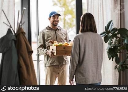 food shipping and people concept - happy delivery man giving wooden box with groceries to female customer at home. food delivery man giving order to female customer