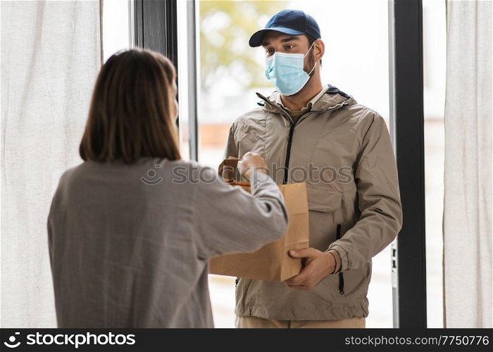 food shipping, pandemic and people concept - delivery man in mask with paper bag giving order to female customer at home. food delivery man in mask giving order to customer