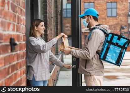 food shipping, pandemic and people concept - delivery man in mask with thermal insulated bag giving order to happy smiling female customer at home. food delivery man in mask giving order to customer
