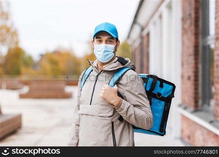 food shipping, pandemic and people concept - delivery man in protective medical mask with thermal insulated bag in city. delivery man in mask with thermal bag in city