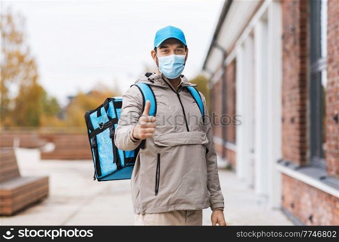 food shipping, pandemic and people concept - delivery man in protective medical mask with thermal insulated bag in city showing thumbs up. delivery man in mask with thermal bag in city