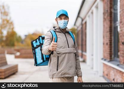 food shipping, pandemic and people concept - delivery man in protective medical mask with thermal insulated bag in city showing thumbs up. delivery man in mask with thermal bag in city