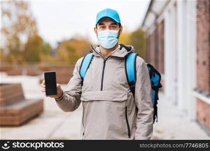 food shipping, pandemic and people concept - delivery man in protective medical mask with thermal insulated bag showing smartphone in city. delivery man in mask with phone and thermal bag