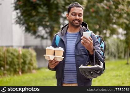food shipping, profession and people concept - happy smiling delivery man with thermal insulated bag and takeaway coffee cups using smartphone on city street. food delivery man with takeaway coffee and phone