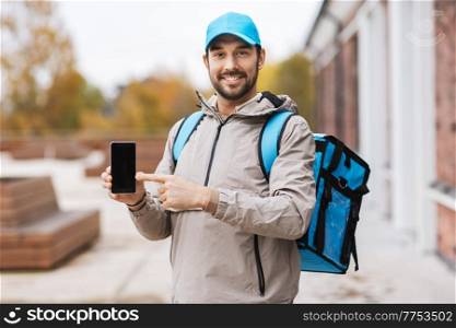 food shipping, profession and people concept - happy smiling delivery man with thermal insulated bag showing smartphone in city. delivery man with phone and thermal bag in city