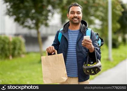 food shipping, profession and people concept - happy smiling delivery man with thermal insulated bag using smartphone on city street. delivery man with takeaway food in bag and phone
