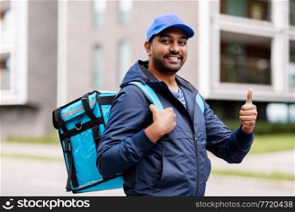 food shipping, profession and people concept - happy smiling indian delivery man with thermal insulated bag showing thumbs up on city street. indian delivery man with bag showing thumbs up