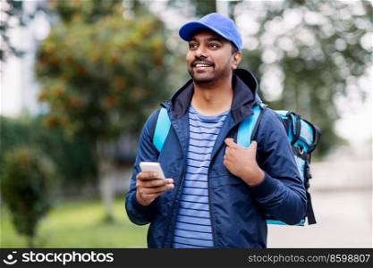 food shipping, profession and people concept - happy smiling indian delivery man with thermal insulated bag and smartphone on city street. smiling indian delivery man with bag and phone
