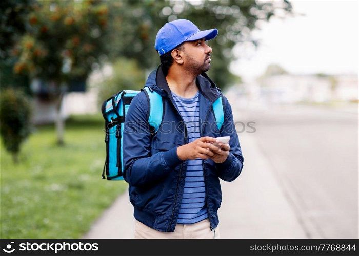 food shipping, profession and people concept - indian delivery man with thermal insulated bag and smartphone on city street. indian delivery man with bag and phone