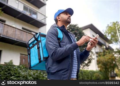 food shipping, profession and people concept - indian delivery man with thermal insulated bag and smartphone on city street. indian delivery man with bag and phone