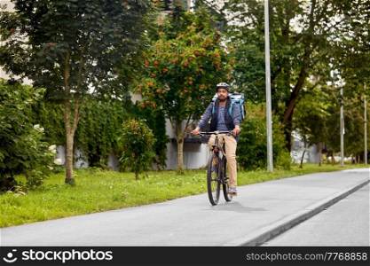 food shipping, transportation and people concept - delivery man in bike helmet with thermal insulated bag riding bicycle on city street. food delivery man with bag riding bicycle