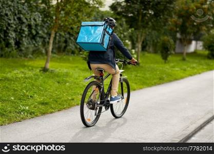 food shipping, transportation and people concept - delivery man in bike helmet with thermal insulated bag riding bicycle on city street. food delivery man with bag riding bicycle