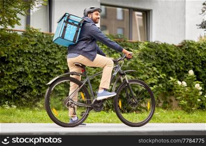 food shipping, transportation and people concept - happy smiling delivery man in bike helmet with thermal insulated bag riding bicycle on city street. food delivery man with bag riding bicycle