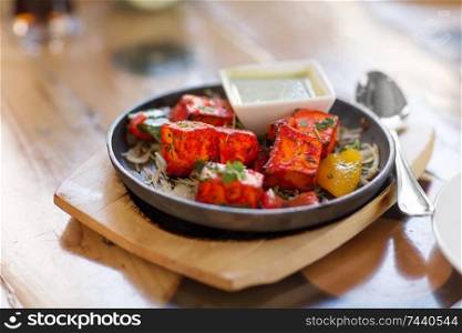 food, south asian cuisine, culinary and cooking concept - close up of paneer tikka chunks with bowl of dip sauce on table of indian restaurant. close up of paneer tikka dish with sauce on table