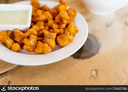 food, south asian cuisine, culinary and cooking concept - close up of cauliflower pakora with dip sauce on table of indian restaurant. close up of cauliflower pakora with dip sauce