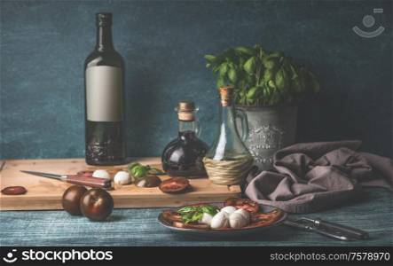 Food still life with oil bottles, mozzarella, tomatoes and kitchen herbs in pot on kitchen table background