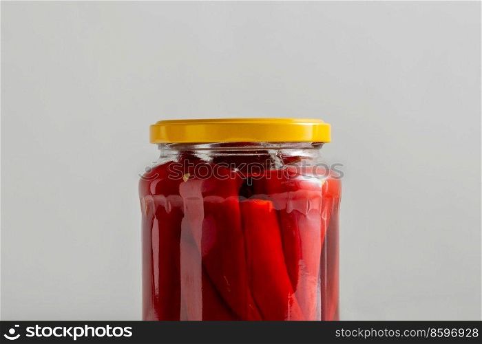 food, storage and preserve concept - close up of jar with pickled red hot chili peppers on grey background. close up of jar with pickled red hot chili peppers