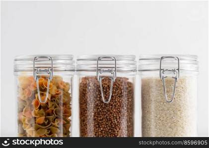 food storage, eating and cooking concept - close up of jars with buckwheat, rice and pasta on white background. close up of jars with buckwheat, rice and pasta