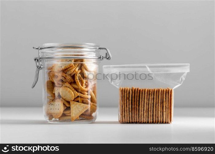 food storage, eating and snacks concept - close up of salted cookies or crackers in jar and plastic bag on white table. salted cookies or crackers in jar and plastic bag