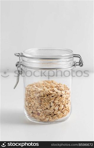 food storage, healthy eating and diet concept - jar with oat flakes on white background. close up of jar with oat flakes on white table