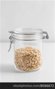 food storage, healthy eating and diet concept - jar with oat flakes on white background. close up of jar with oat flakes on white table