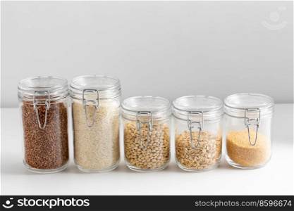 food storage, healthy eating and diet concept - jars with buckwheat, rice, oat flakes, couscous and beans on white background. jars with buckwheat, rice, oat, couscous and beans