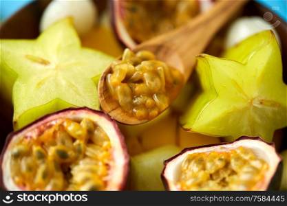 food, summer and healthy eating concept - close up of different exotic fruits mix in plate with wooden spoon. close up of of exotic fruits mix with wooden spoon