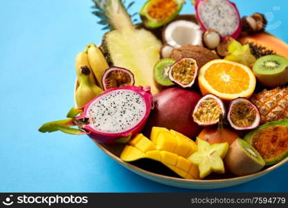 food, summer and healthy eating concept - close up of plate of different exotic fruits on blue background. plate of exotic fruits on blue background