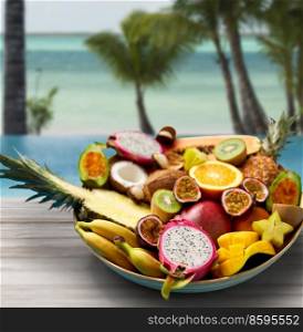 food, summer and healthy eating concept - close up of plate of different exotic fruits on tropical beach background. plate of exotic fruits on tropical beach