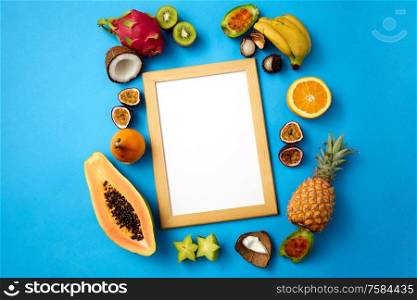 food, summer and healthy eating concept - different exotic fruits around wooden frame with blank white template on blue background. fruits around wooden frame with white background