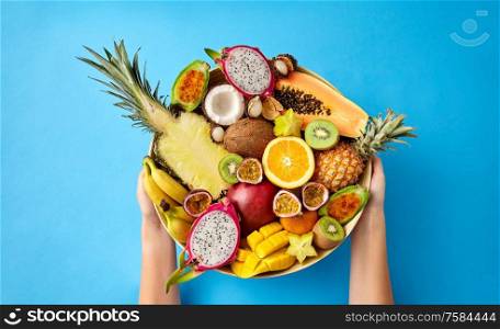 food, summer and healthy eating concept - hands holding plate of different exotic fruits on blue background. hands holding plate of exotic fruits over blue