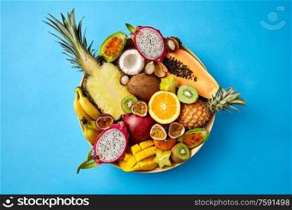 food, summer and healthy eating concept - plate of different exotic fruits on blue background. plate of exotic fruits on blue background