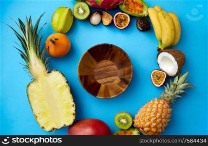food, summer and healthy eating concept - wooden plate or bowl and different exotic fruits on blue background. wooden bowl and different exotic fruits on blue