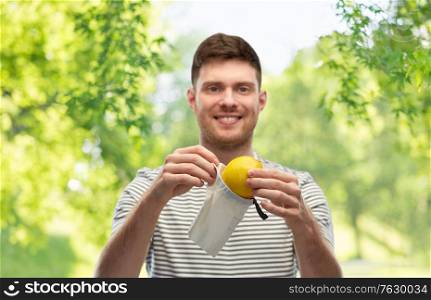 food, sustainability and eco living concept - smiling young man in striped t-shirt with lemon in reusable canvas bag over green natural background. smiling man with lemon in reusable canvas bag