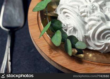 food, sweets and objects concept - close up of meringue or zephyr cake on wooden stand with eucalyptus branch over dark background. close up of zephyr cake on wooden stand