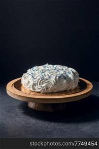 food, sweets and objects concept - meringue or zephyr cake with blue sprinkles on wooden stand over dark background. close up of zephyr cake on wooden stand