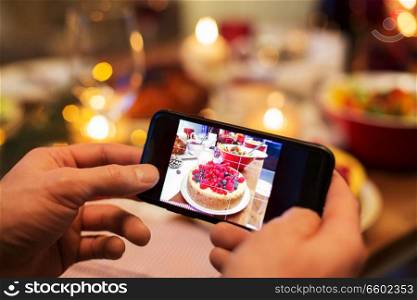 food, technology and holidays concept - close up of male hands photographing cake by smartphone at christmas dinner. hands photographing food at christmas dinner