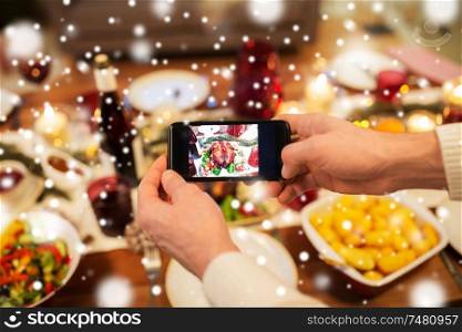 food, technology and holidays concept - close up of male hands photographing roast turkey by smartphone at christmas dinner over snow. hands photographing food at christmas dinner