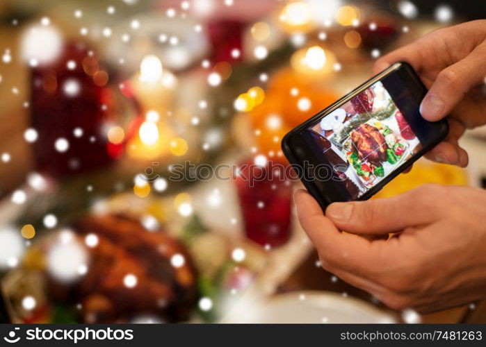 food, technology and holidays concept - close up of male hands photographing roast turkey by smartphone at christmas dinner over snow. hands photographing food at christmas dinner