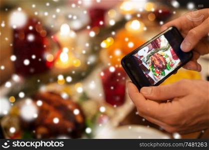 food, technology and holidays concept - close up of male hands photographing roast turkey by smartphone at christmas dinner over snow. hands photographing food at christmas dinner